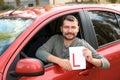 Man showing learner driver sign from new car.