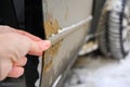 A man shows rust on a car door from winter reagents.