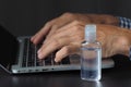 Man shows small bottle antibacterial sanitizer gel for disinfect hands near laptop.