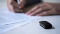 Man signs papers on car purchase or rent, auto insurance services, key on table