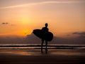 Man silhouette holding surfing board, walking on dark seashore. Surfer standing on sunset sky over the sea water background. Royalty Free Stock Photo