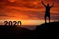 Man silhouette on the mountain top watching the sunrise and 2020 years while celebrating