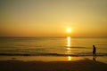 A man silhouette walking barefoot on sand beach at morning sunrise scene with sea view, wave water reflection