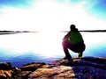 Man sit at evening sea. Hiker with backpack sit in squatting position along beach. Royalty Free Stock Photo