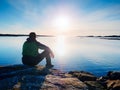 Man sit at evening sea. Hiker with backpack sit in squatting position along beach. Royalty Free Stock Photo