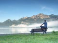 Man sit lone on bench in park next lake. Mountain range