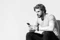 Man sit with smartphone on grey wall, new technology. Macho with beard, blond hair in tshirt on sunny day, fashion. New