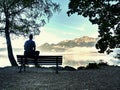 Man sit on wooden bench at coast of lake bellow blue mountains Royalty Free Stock Photo