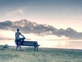 Man sit on wooden bench at coast of lake bellow blue mountains Royalty Free Stock Photo