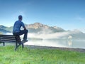 Man sit on wooden bench at coast of lake bellow blue mountains Royalty Free Stock Photo