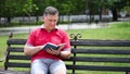 A man sits on a bench in a city park and works on a tablet