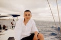 A man sits on the bow of a sailing yacht and enjoys life. Handsome guy in a white shirt, businessman, freelancer resting in the se Royalty Free Stock Photo