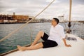 A man sits on the bow of a sailing yacht and enjoys life. Handsome guy in a white shirt, businessman, freelancer resting in the se Royalty Free Stock Photo