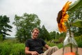 A man sits on a chair smiling in a grass field with a sunflower in a vase Royalty Free Stock Photo