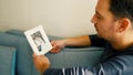 a man sits on the couch and looks pensively at his wedding photo and digests it face down