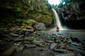 Man sits cross legged on rocks beneath waterfall