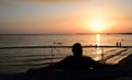 A man sits in front and with his back to the photographer and looks with outstretched arms forward to the horizon of the sea,