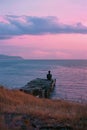 A man sits on the grassy hill overlooking an old pier that is floating in the ocean Royalty Free Stock Photo