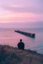 A man sits on the grassy hill overlooking an old pier that is floating in the ocean Royalty Free Stock Photo