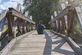 The man sits with his back turned on an old wooden bridge Royalty Free Stock Photo