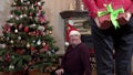 A man sits near a Christmas tree and a woman stands in front of him and holds a sealed Christmas present behind his back Royalty Free Stock Photo