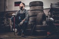 A man sits on an old tire in a garage.