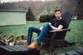 Man sits outdoors on a wooden chair on the backyard of his house at rural area.