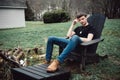 Man sits outdoors on a wooden chair on the backyard of his house at rural area.