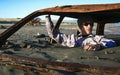 Man sits in rusted car wreck buried in sand on beach Royalty Free Stock Photo