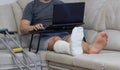 A man sits on a sofa in a cast with a laptop.