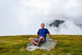 The man sits on a stone surrounded by fog and low clouds near Transalpina road in Romania Royalty Free Stock Photo