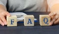 Man sits at a table and holds cubes. inscription FAQ frequently asked questions on wooden blocks on a blue background Royalty Free Stock Photo