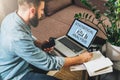 Man sits at table,working, uses laptop with inscription statistical analysis on screen and makes notes in his notebook.