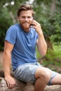 man sits on tree trunk in forest using mobile phone Royalty Free Stock Photo