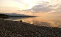 A man sitting alone on a log at the over the edge of a sea, dawn silence on lake. Royalty Free Stock Photo