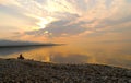 A man sitting alone on a log at the over the edge of a sea, dawn silence on lake. Royalty Free Stock Photo