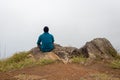 Man sitting alone at mountain rock with white mist background from flat angle