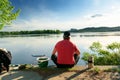 Man sitting alone near calm lake fishing on sunny day. Mental relaxation and contemplation of nature. Fishing hobby Royalty Free Stock Photo