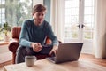 Man Sitting On Armchair At Home With Laptop Making Online Purchase With Credit Or Debit Card Royalty Free Stock Photo