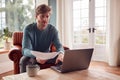 Man Sitting On Armchair At Home With Laptop Paying Bill Online