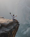 Man sitting atop a rocky cliff with his hands raised.