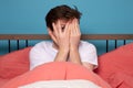 Man sitting on bed peeping through fingers, frightened