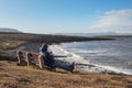 Man sitting on a bench with a beautiful view on Atlantic ocean and looking on the screen of his smart phone,