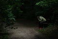 Man sitting on a bench in light spot on forest path, surrounded with darkness, covering his face with his hands Royalty Free Stock Photo