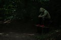 Man sitting on a bench in light spot on forest path, surrounded with darkness, green hoodie covering his face Royalty Free Stock Photo