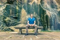 Man sitting on a stone bench and thinking with his back to a waterfall Royalty Free Stock Photo