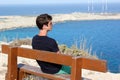 Young Man sitting on bench on sunny day and looking to ocean and sky horizon. Man relaxing under hot sun and after day walking.