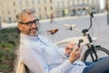 Man sitting bench and using cellphone in city. bicycle in background Royalty Free Stock Photo