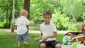 Man sitting on blanket with children in park. Children playing with soap bubbles Royalty Free Stock Photo