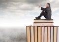 Man sitting on Books stacked by grey cloudy sky Royalty Free Stock Photo